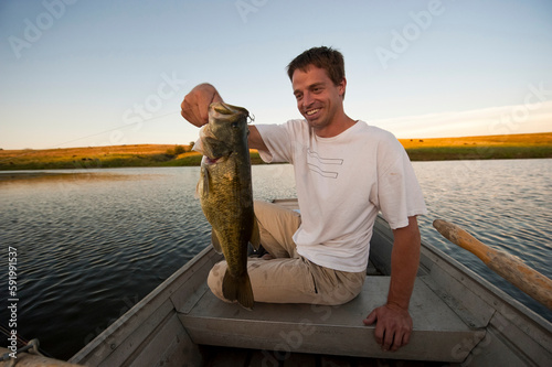 Man holds a fresh caught fish in a rowboat; Valparaiso, Nebraska, United States of America