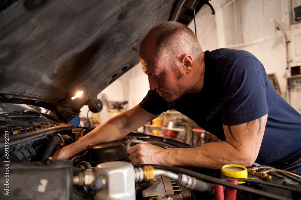 Mechanic checks a car's engine inside an auto shop; Lincoln, Nebraska, United States of America Mechanic checks a car's engine inside an auto shop; Lincoln, Nebraska, United States of America