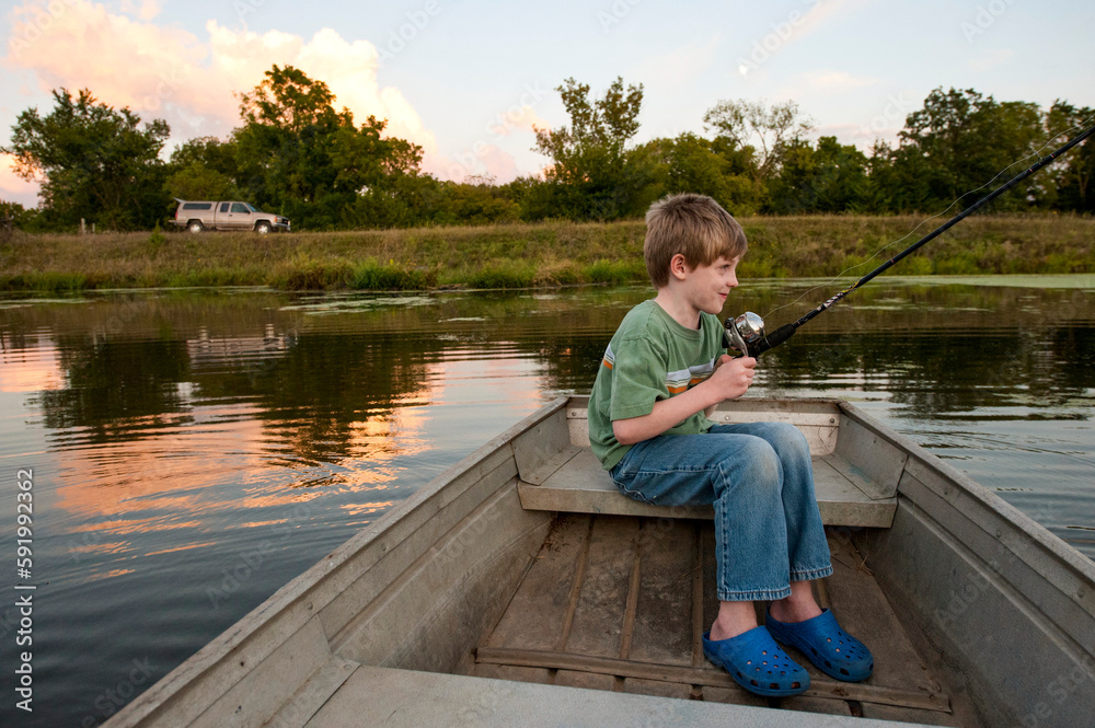 Young boy anticipates catching a fish in a pond from a boat at dusk; Ceresco, Nebraska, United States of America Young boy anticipates catching a fish in a pond from a boat at dusk; Ceresco, Nebraska, United States of America