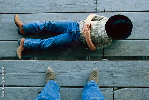 Young cowboy has a nap on the grandstands, face covered by a hat and a pair of clad feet; Burwell, Nebraska, United States of America photo