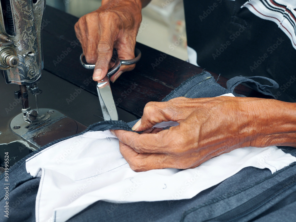 Elderly man hands fixing the pant and cutting the thread on the sewing machine close-up.