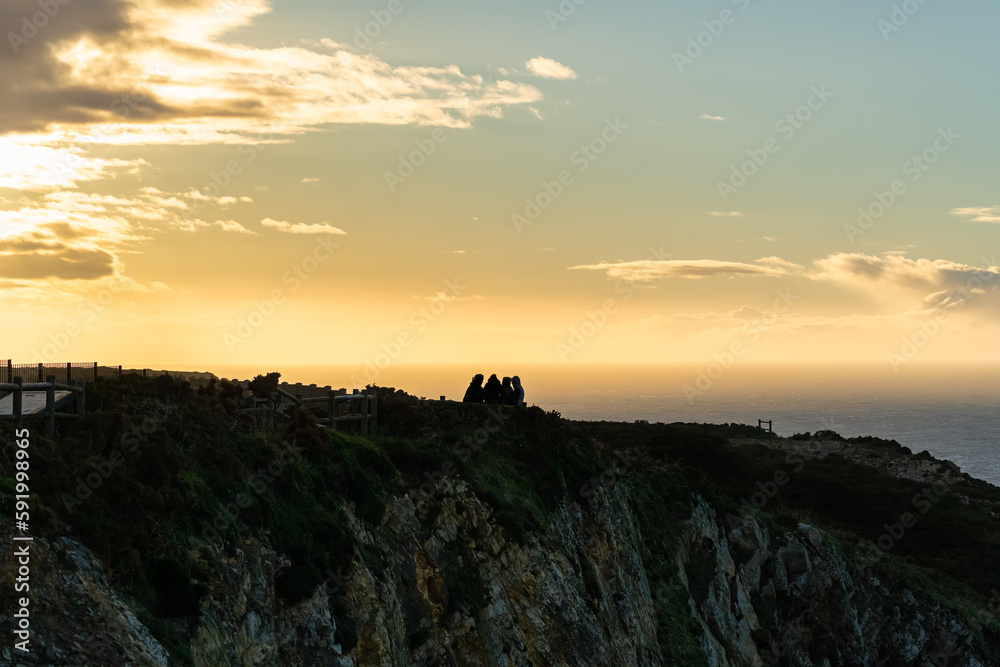 Sunset over the cliffs on the seashore with a group of people in silhouette enjoying the views, Asturias.