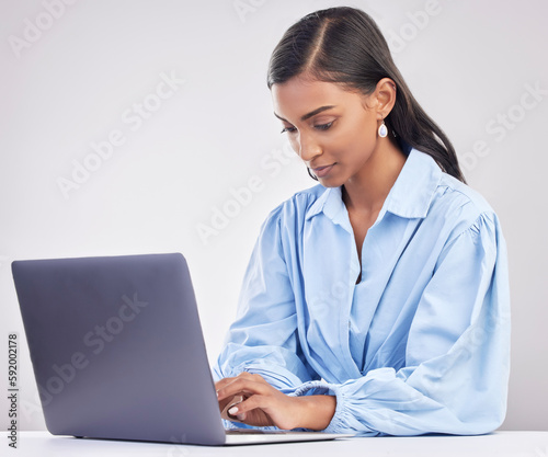 Laptop, research and woman typing in a studio while working on an online corporate project. Focus, technology and professional female employee planning business report on computer by gray background.