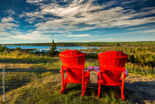 Two large red chairs with the warm light at sunset on a field overlooking a river valley with dramatic clouds and blue sky; Calgary, Alberta, Canada