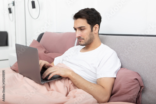 Handsome man lying on the bed and working on laptop in the bedroom  © Vitaliy