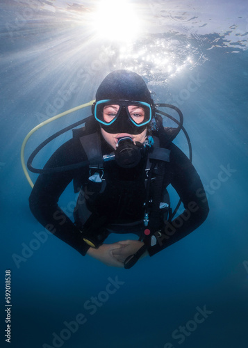 Closeup of a happy scuba diver underwater facing the camera with the bright sunrays shining through the water surface behind her