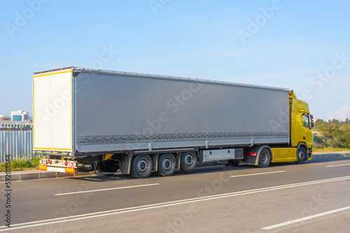 Truck yellow with a large trailer under an awning stop on the side of the road.
