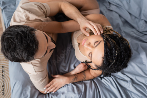 top view of passionate african american woman in lingerie and man in t-shirt embracing in bedroom at home.