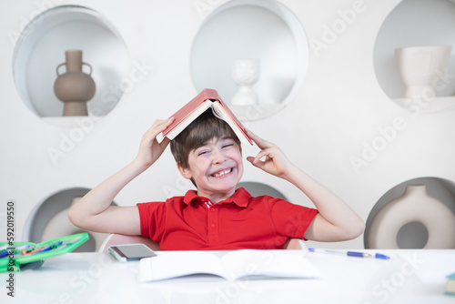 Cute happy school boy sits at the desk and learns his lessons