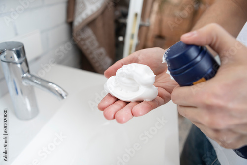 Man squeezing shaving foam from tube in the bathroom. Shaving and morning routine concept 