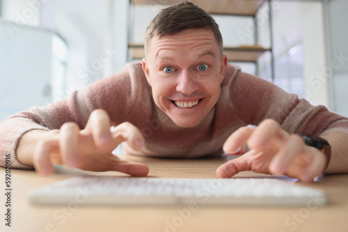 Crazy man types on keyboard with fingers looking with smile