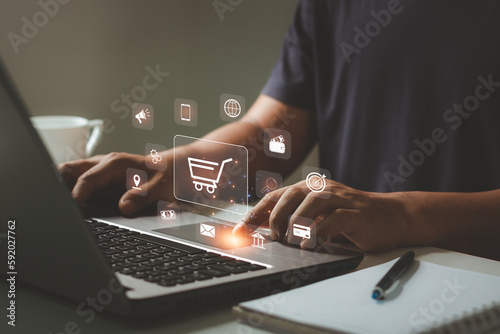 Online shopping and e-commerce concept. Young man using laptop computer with shopping cart icon, order in online store, shopping on internet, concept on virtual screen with hands typing on keyboard.