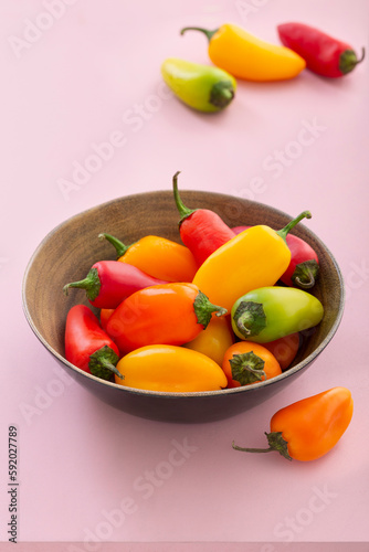 colored chili peppers in a rustic wooden pot on a pink background