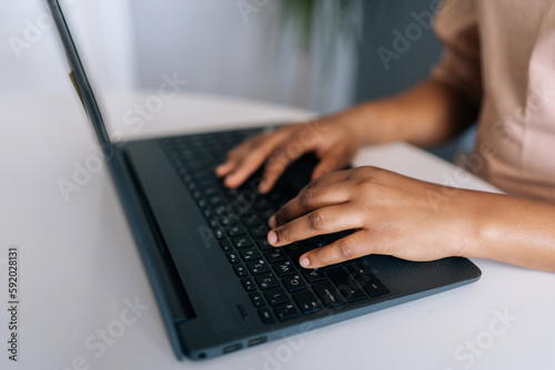 Close-up cropped shot of unrecognizable African-American freelancer in casual clothes working typing on laptop computer from remote home office, sitting at desk, close up, side view, selective focus.