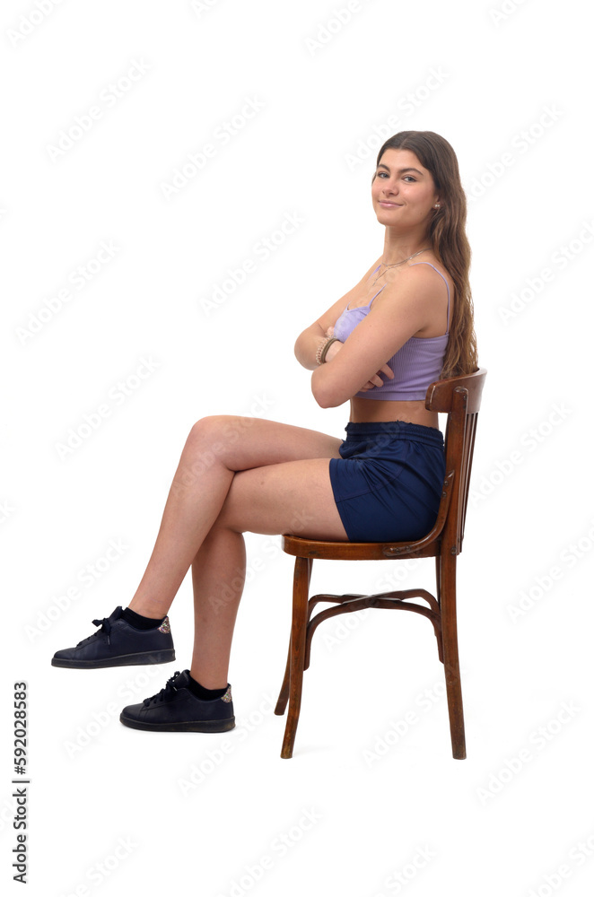 side view of a young girl sitting on chair looking at camera and cross legged and arms crossed on white background side view of a young girl sitting on chair looking at camera and cross legged and arms crossed on white background