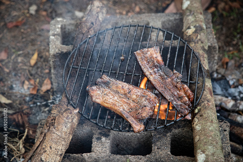 Chunks of pork ribs roasting on improvised block grill in camp. Rustic outdoor barbecue.
