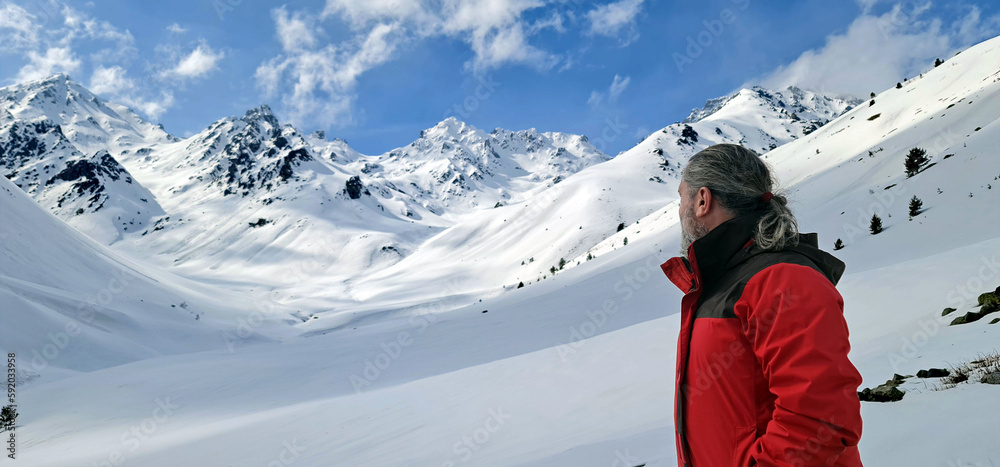 mountaineer man in red jacket looking towards snowy mountains in a valley