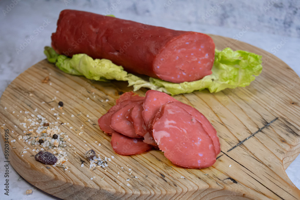 Vegan salami sausage made with washed flour and bits og vegan cheese fat, sliced on wooden board Vegan salami sausage made with washed flour and bits og vegan cheese fat, sliced on wooden board