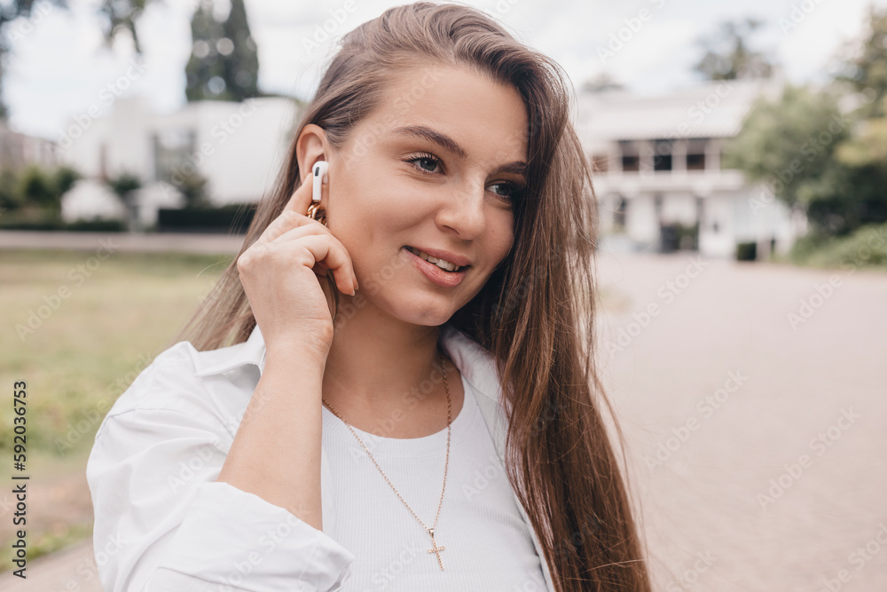 Relaxed young woman brunette in wireless headphones walk on the street listening to music. Enjoying listening to lounge music live via smartphone app, relaxed, eyes closed, laughing, touch earphones. Relaxed young woman brunette in wireless headphones walk on the street listening to music. Enjoying listening to lounge music live via smartphone app, relaxed, eyes closed, laughing, touch earphones.