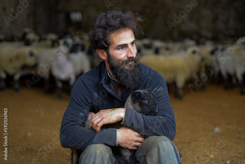 Tela portrait of a breeder with a lamb in his arms inside a barn