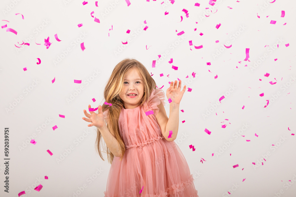little girl blonde in a pink dress catches confeti smiling happy on white background, holiday concept. A child is celebrating a birthday on a white background