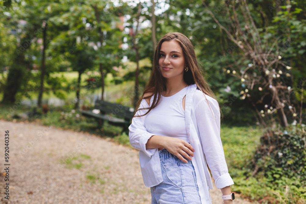 Attractive brunette woman walk on the countryside street. Girl wear white shirt and top and look happy and smiles. Woman walk on the street, she turn around and look joy, flying long hair. Side view.