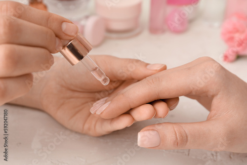 Manicure master applying cuticle oil onto female fingernails on light background  closeup