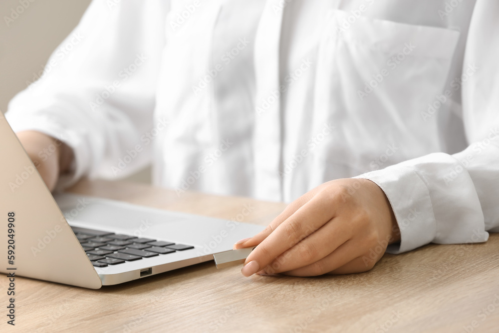 Woman using USB flash drive with modern laptop at wooden table, closeup Woman using USB flash drive with modern laptop at wooden table, closeup