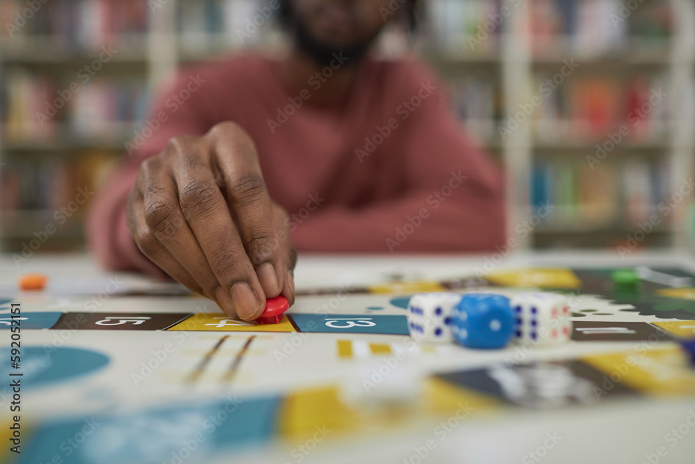 Fototapeta premium Closeup of black man playing board game with focus on male hand moving game piece, copy space