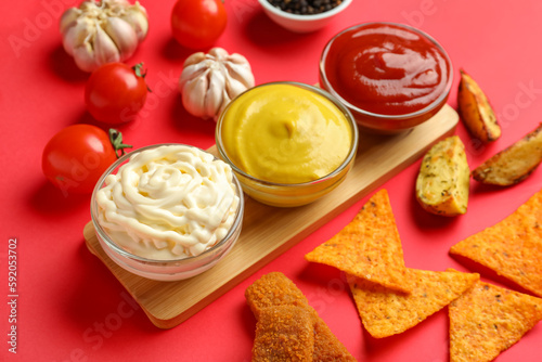 Composition with different sauces, snacks and vegetables on red background