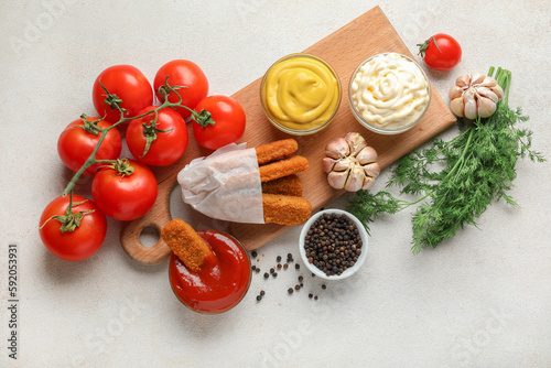 Composition with different sauces, fish nuggets and vegetables on white table