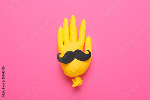 Inflated rubber glove with paper moustache on pink background
