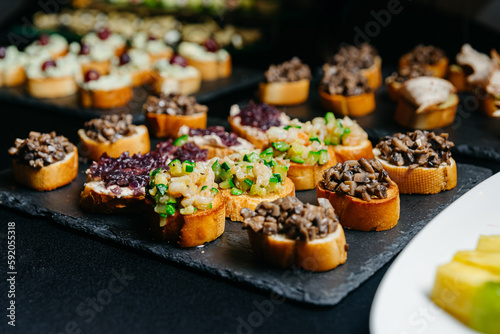 catering, food and drink concept - close up of different bruschettas with diced vegetables and mushrooms on a black slate board