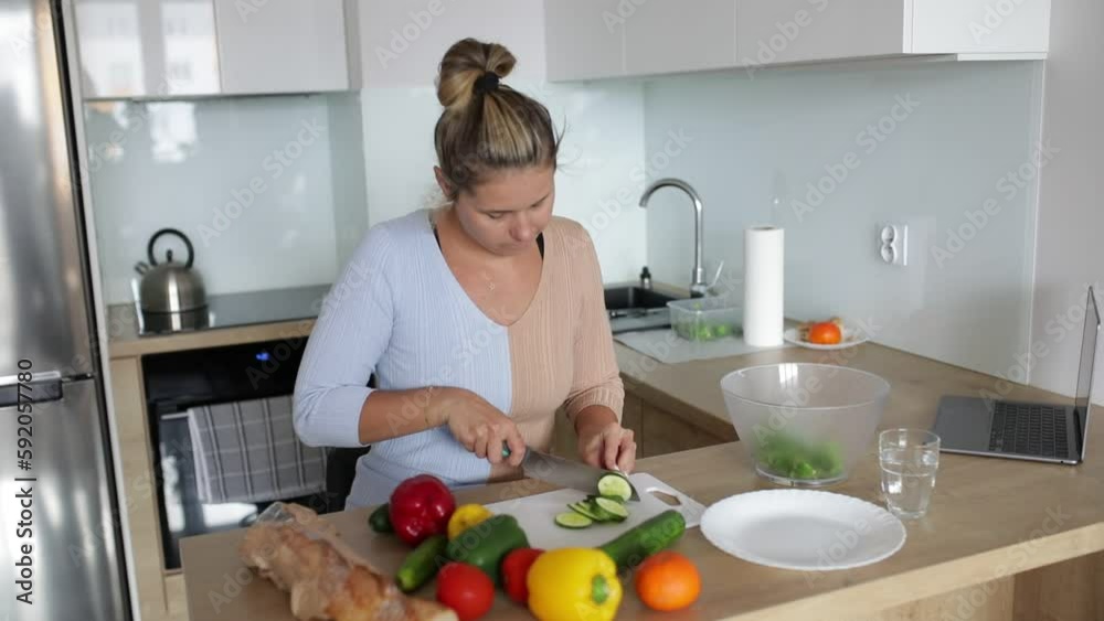 Young pretty woman in is preparing salad of fresh vegetables in her kitchen, slicing cucumber, tomatoes and peppers . Young pretty woman in is preparing salad of fresh vegetables in her kitchen, slicing cucumber, tomatoes and peppers .