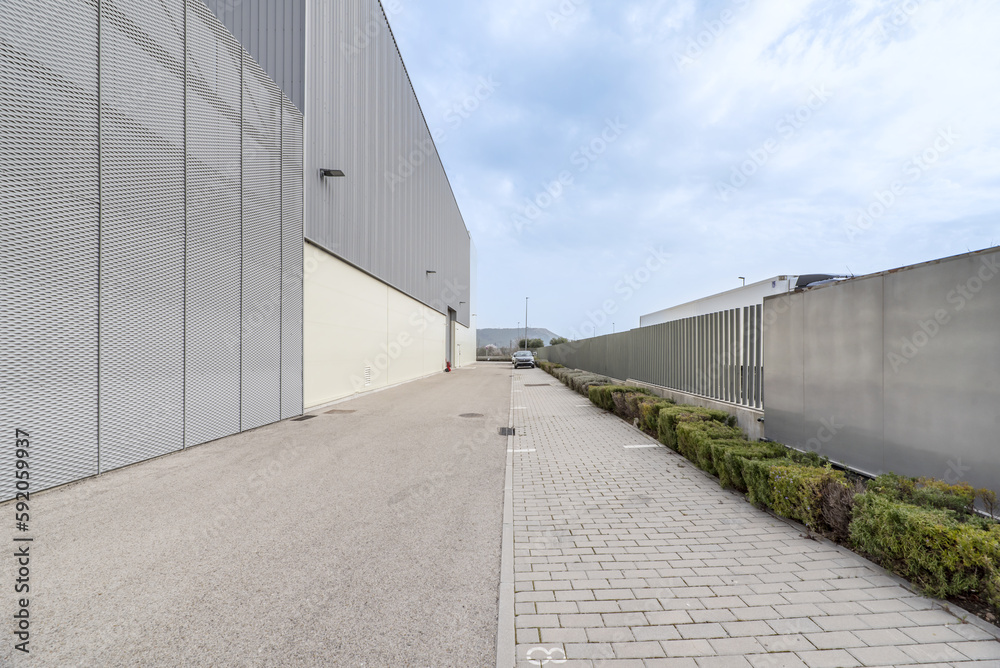 Facade of an industrial warehouse with gardens and parking area for vehicles