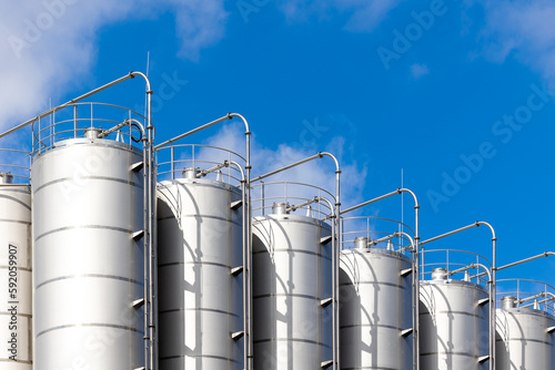 Obraz na płótnie Stainless steel silos against the blue sky. Warehouses for storage of plastics and bulk grains. w salonie