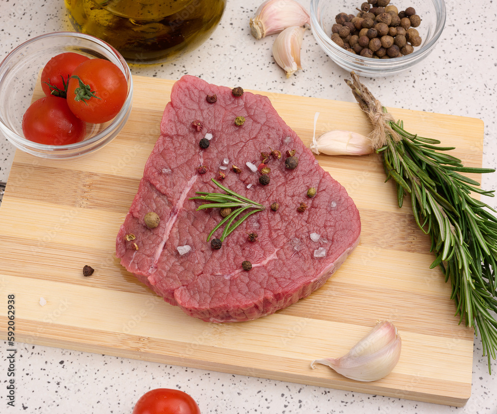 Raw piece of beef with spices pepper, rosemary sprig, salt and olive oil on a wooden board, top view Raw piece of beef with spices pepper, rosemary sprig, salt and olive oil on a wooden board, top view