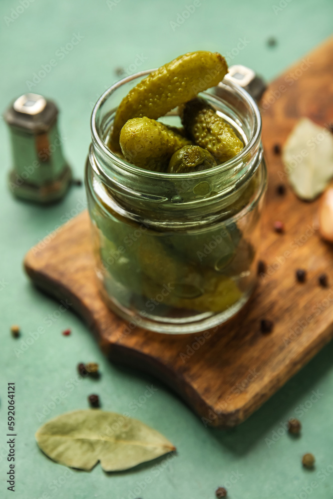 Jar with tasty fermented cucumbers and wooden board on green background