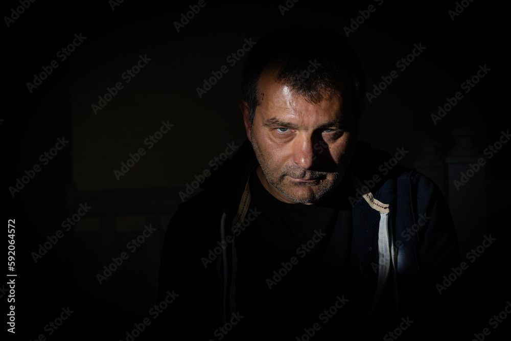 Fototapeta premium A striking portrait captured on a black backdrop with distinct shadows, featuring a male model in his fifties from the Balkan region who is staring directly at the camera with an unshaven face.