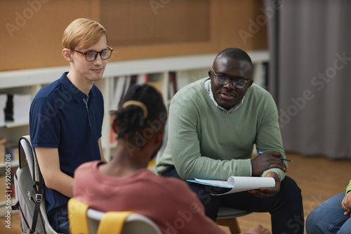 Portrait of black man as male psychologist talking to group teenagers in therapy session