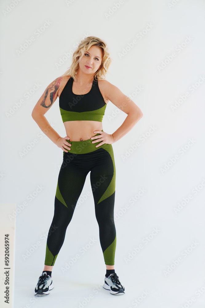 an attractive blonde in a black and green tracksuit poses on a white background. an attractive blonde in a black and green tracksuit poses on a white background.