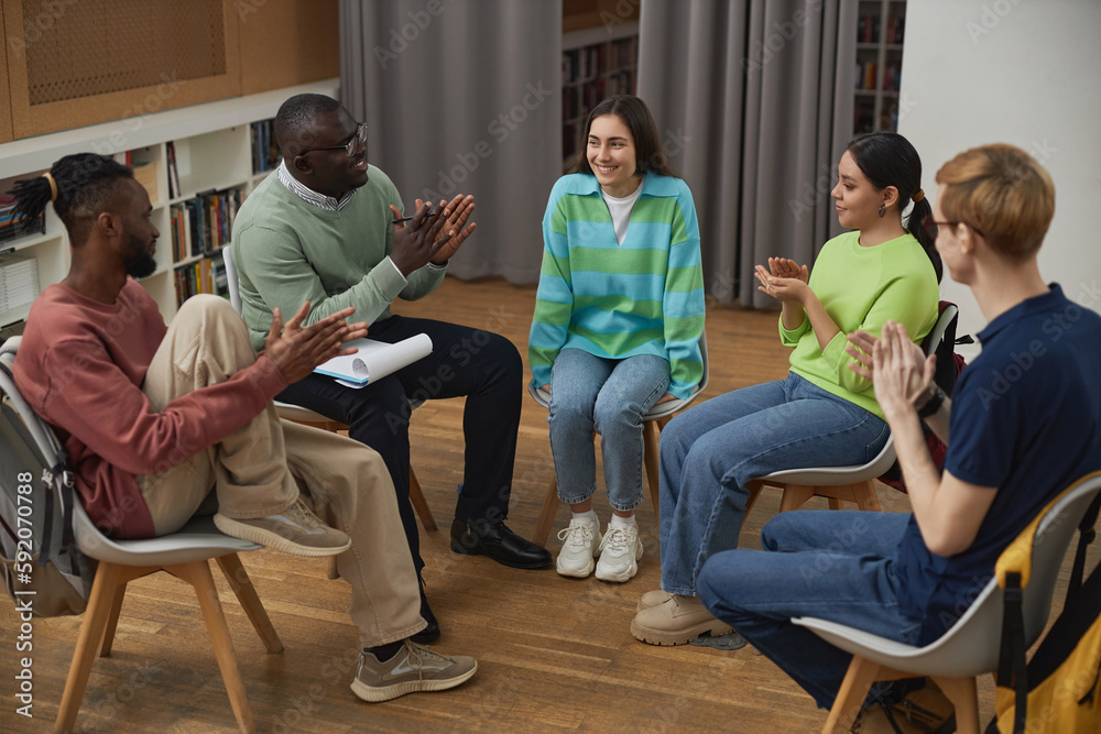 Diverse young people in support group circle applauding to young woman sharing success story Diverse young people in support group circle applauding to young woman sharing success story