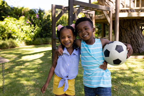 Portrait of smiling african american siblings with soccer ball standing in park