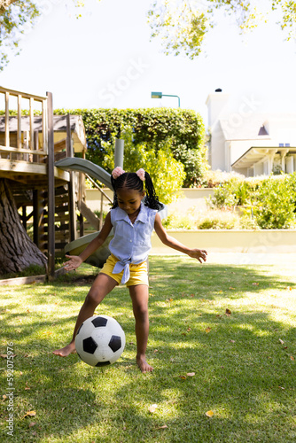Full length of cheerful african american girl playing soccer on grassy field in park