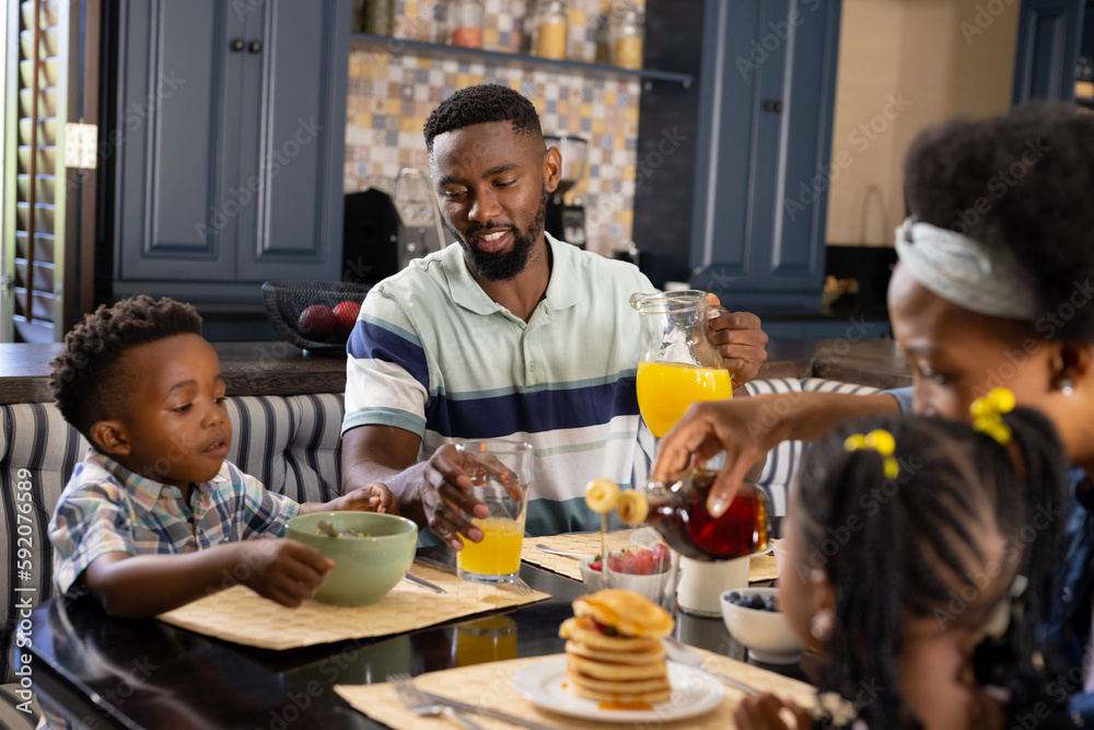 African american parents and children having pancakes and juice on dining table at home