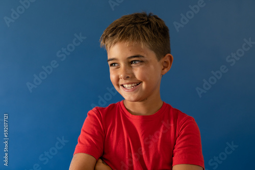 Portrait of caucasian smiling boy looking away while standing on blue background
