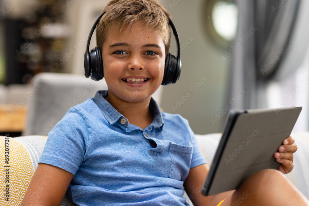 Portrait of caucasian boy wearing headphones and using digital tablet while sitting on sofa at home Portrait of caucasian boy wearing headphones and using digital tablet while sitting on sofa at home