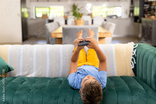 Caucasian boy using mobile phone while lying on sofa in living room, copy space