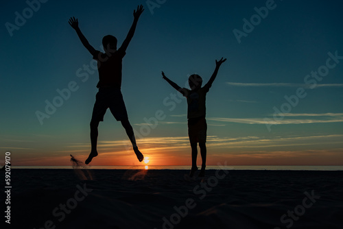 silhouettes of children jumping on a beach during sunset