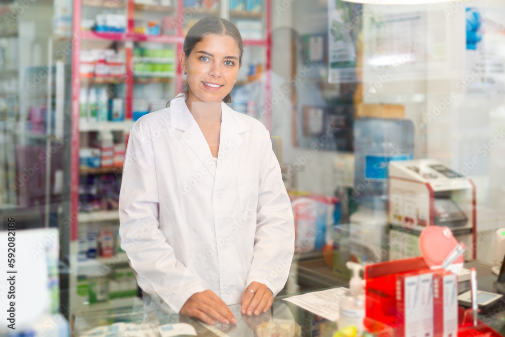 Portrait of a young female pharmacist standing behind the counter of a pharmacy. Close-up portrait